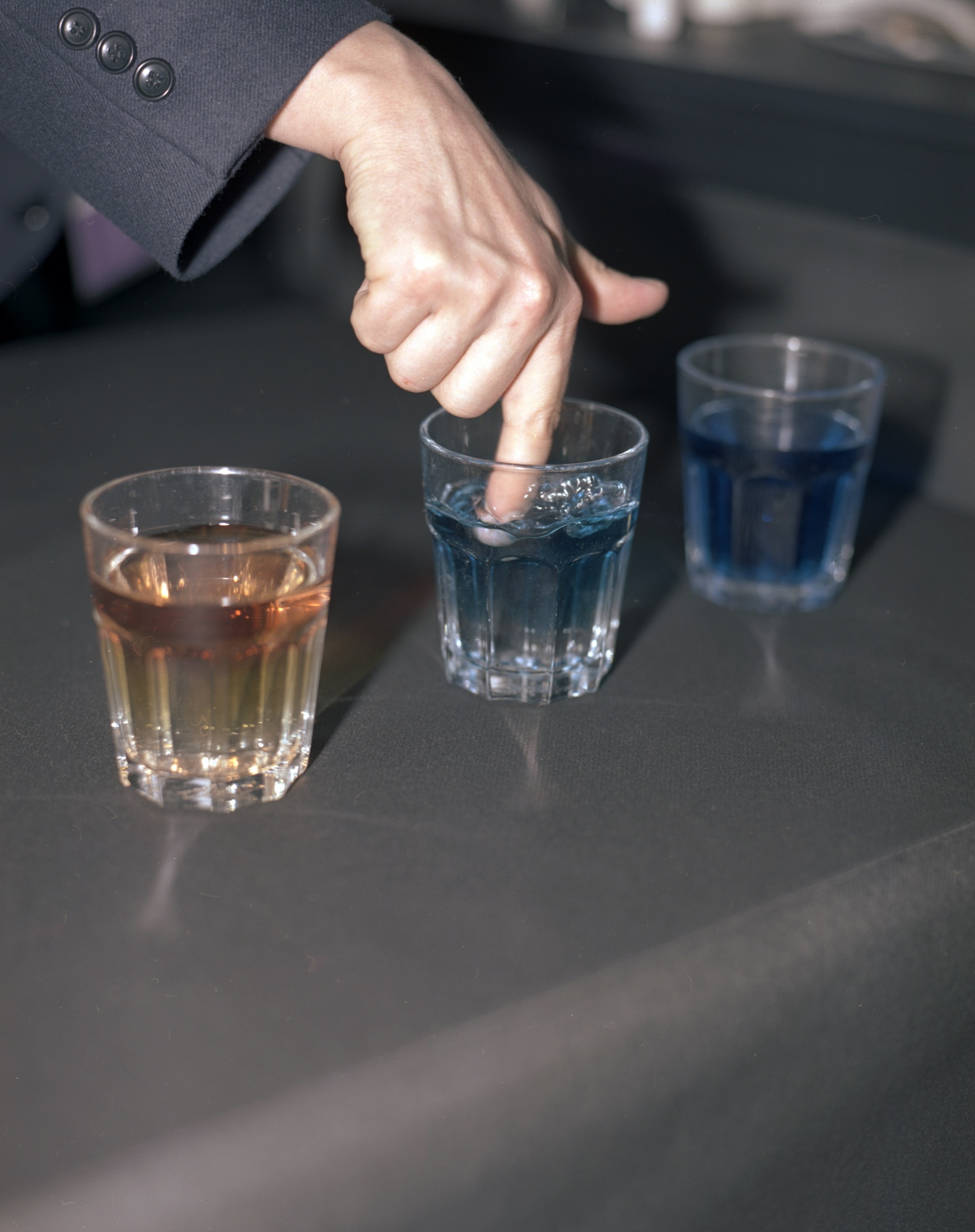 Une main désigne trois verres d'eau colorée sur une table